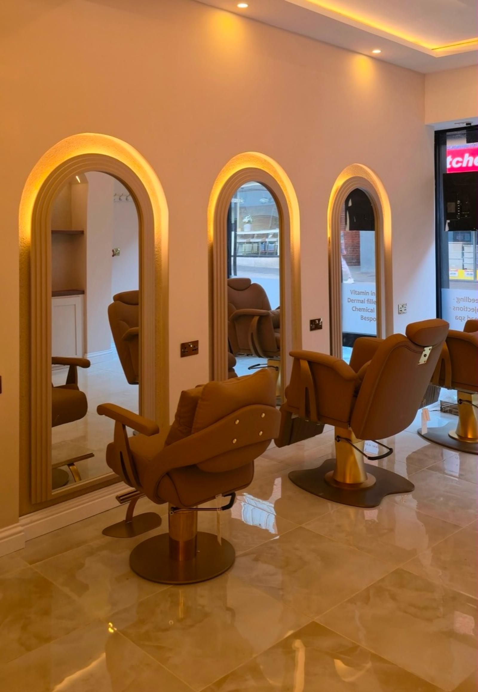 A row of arched, LED-lit mirrors with camel leather salon chairs on a glossy marble floor