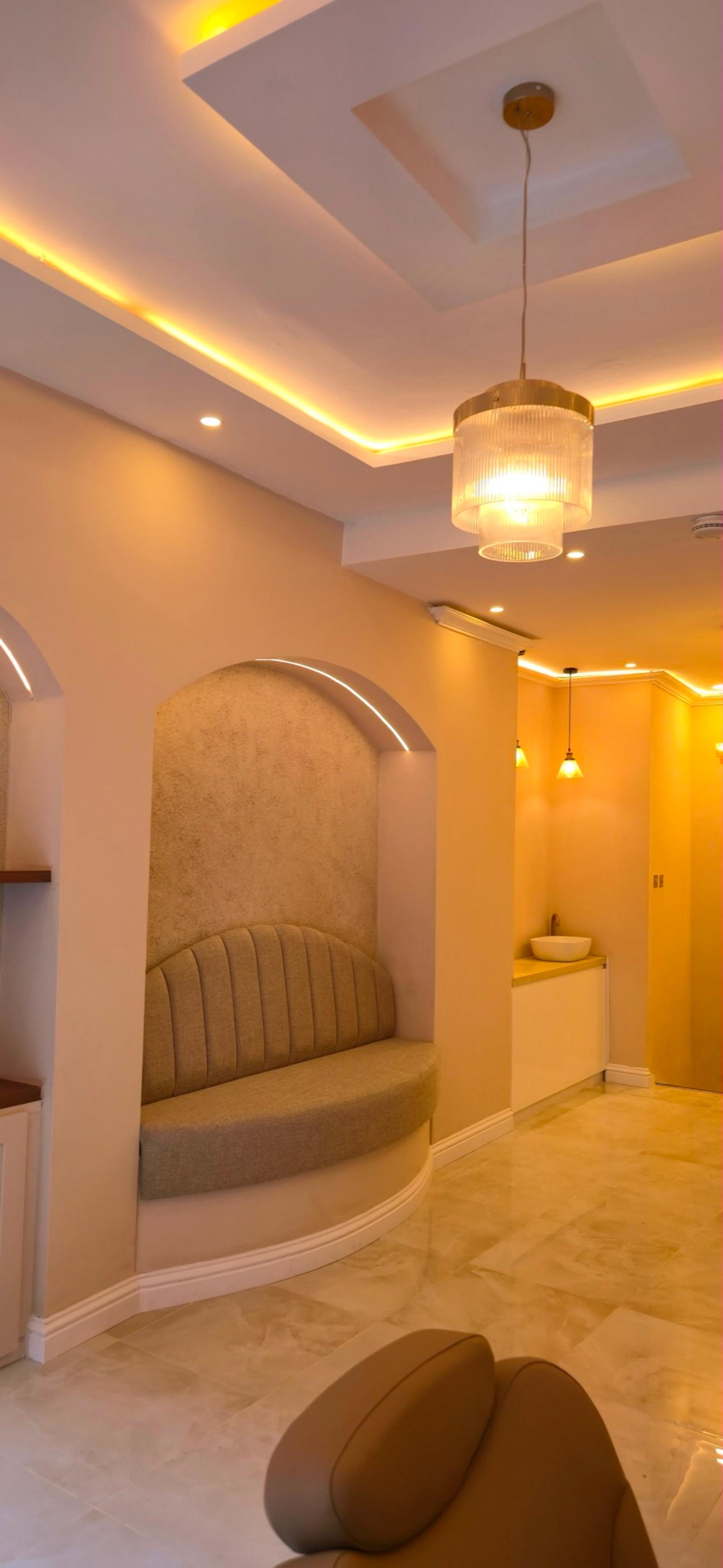 Suede scallop-backed arch seat beneath warm cove lighting and a ribbed-glass pendant